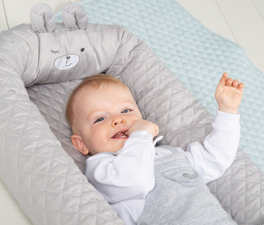 Säugling liegt in grauer Roba Babylounge auf blauer Unterlage.