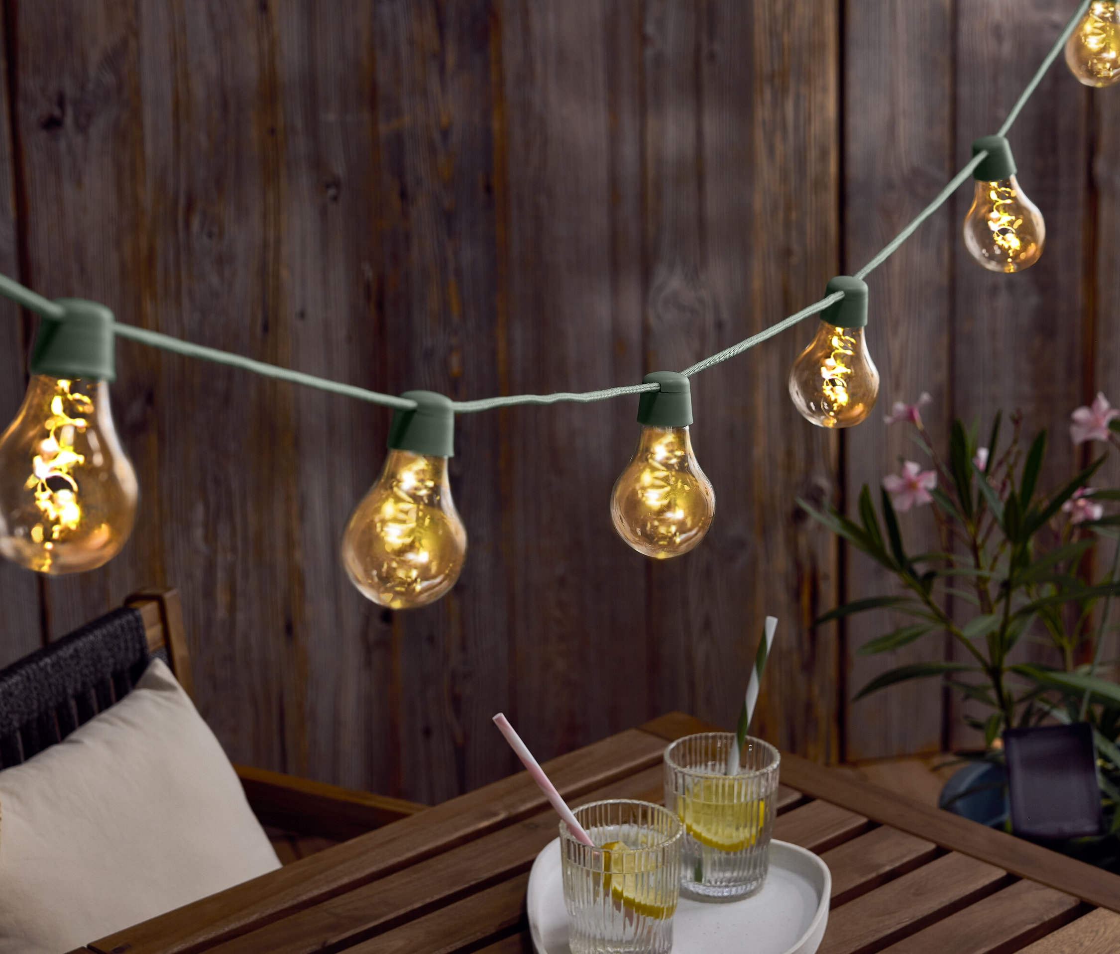 Lichterkette mit Glühbirnen hängt über einem Holztisch mit Getränken und einem Hut.