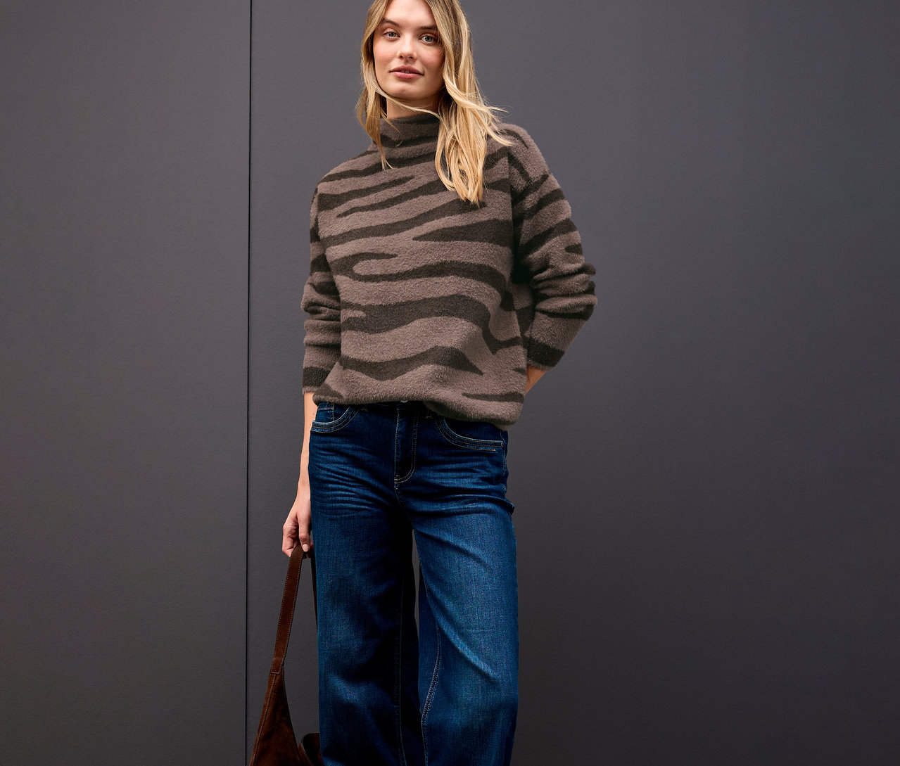 Frau trägt Street One Jacquard-Pullover, Jeans und eine braune Handtasche.