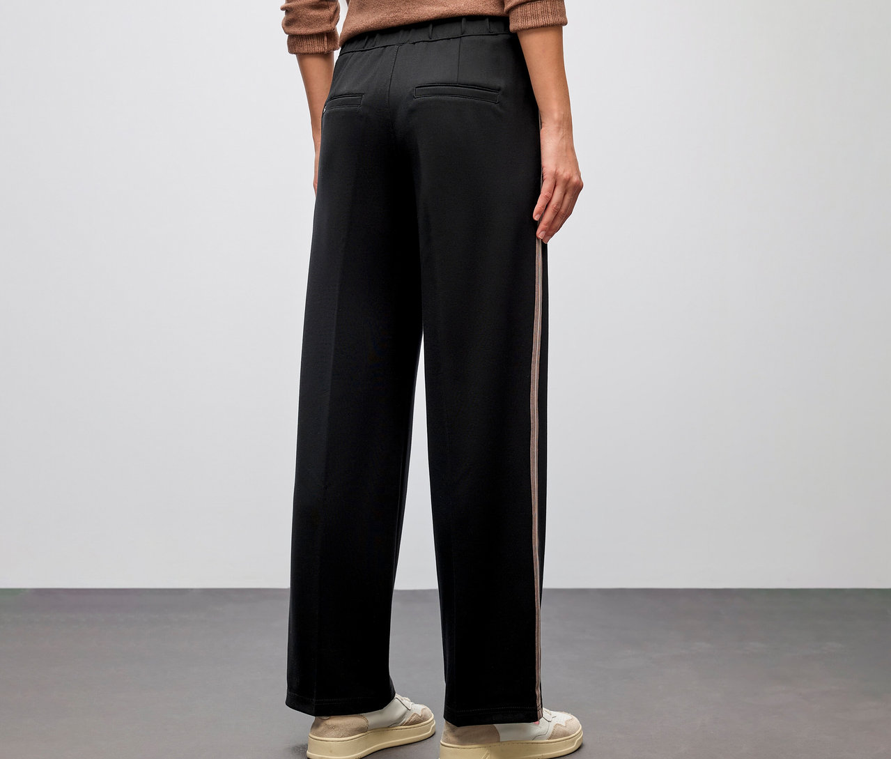 Person von hinten, trägt eine braune Bluse und eine schwarze Street One Straight Leg Hose mit Gallon, dazu cremefarbene Sneaker.