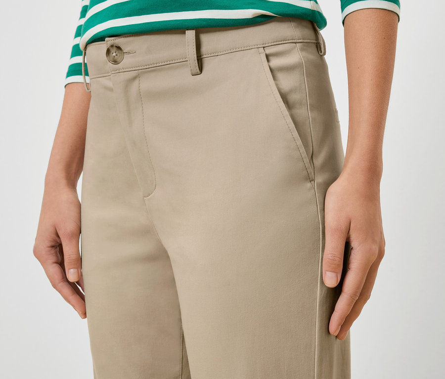 Nahaufnahme einer Frau, die eine beige Hose und ein grün-weiß gestreiftes Oberteil trägt.