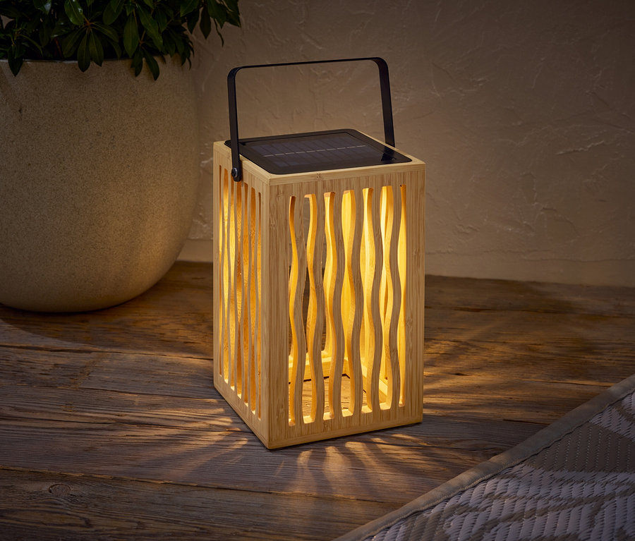 Eine Solarleuchte aus Holz mit einem schwarzen Griff steht auf einem Holztisch neben einem Topf mit einer Pflanze.