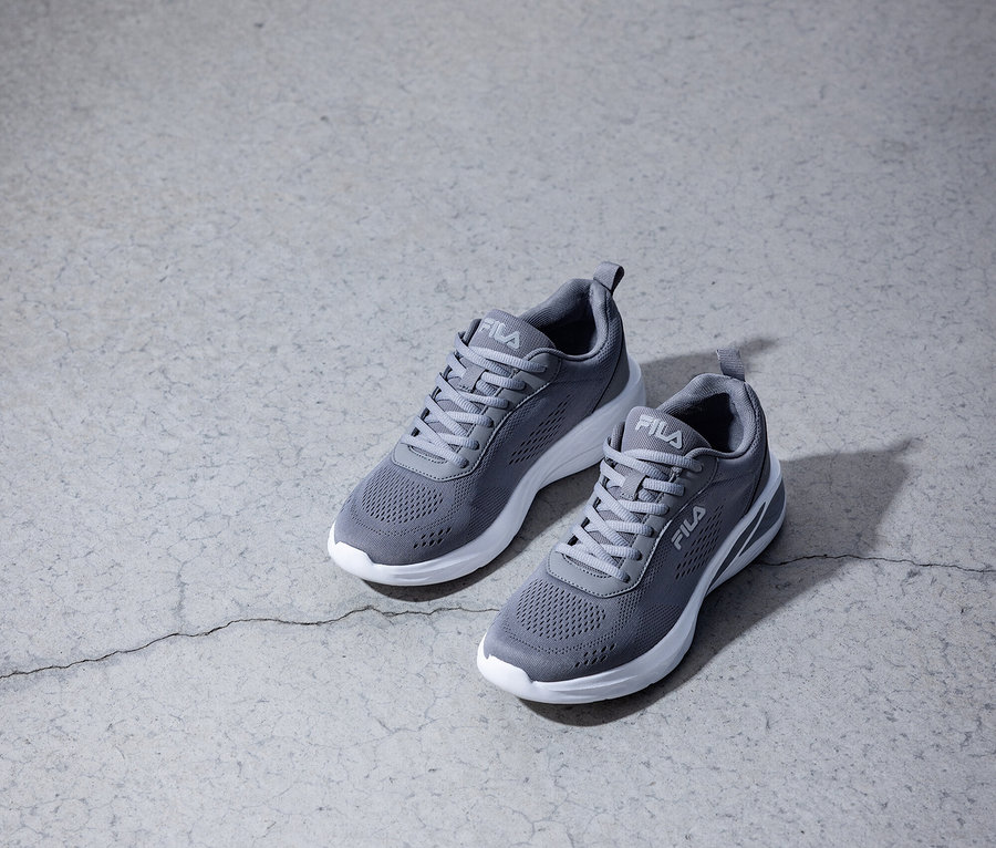 Zwei graue Fila-Sneakers mit weißen Sohlen stehen auf einem grauen Betonboden.