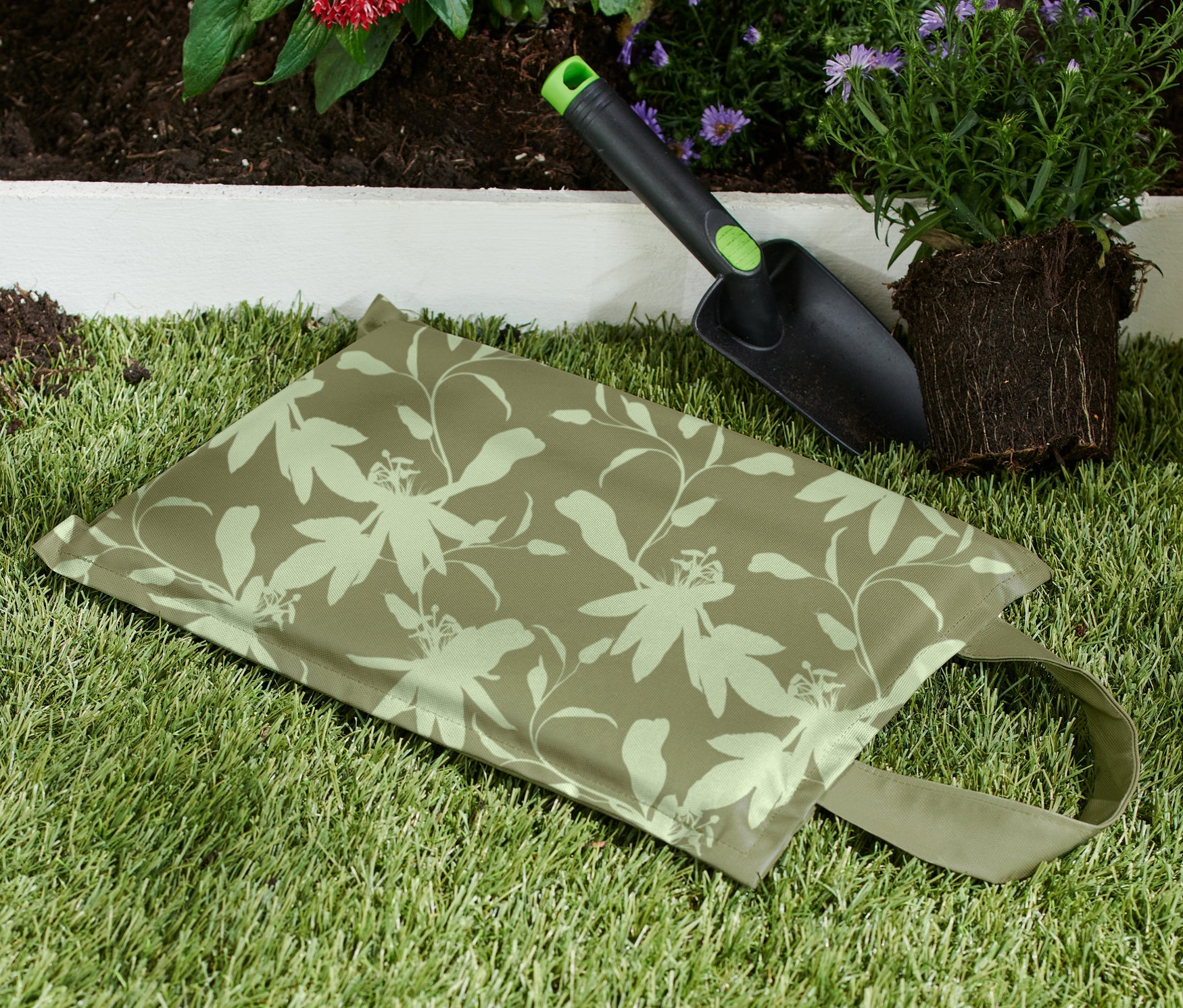 Ein Kniekissen liegt auf dem Rasen neben einer Schaufel und einer Pflanze.