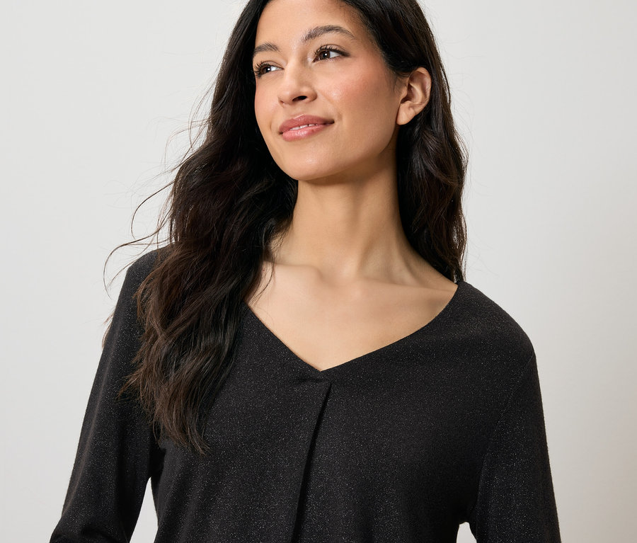 Porträt einer lächelnden Frau mit langen, dunklen Haaren in einem schwarzen, glitzernden Oberteil mit V-Ausschnitt.