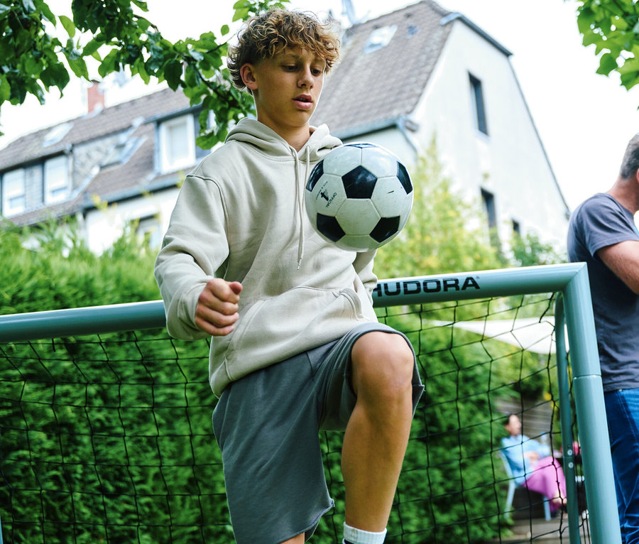 Jugendlicher jongliert einen Fußball mit dem Knie vor einem Hudora Fußballtor »Expert 240« im Garten.