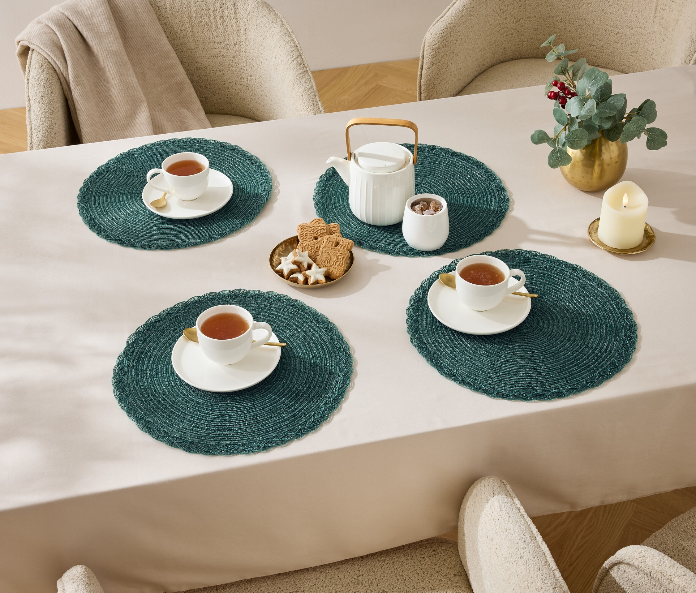 Vier Tassen Tee auf einem Tisch mit einer Tischdecke, Teekanne, Zuckerdose, Kekse und einer Kerze.