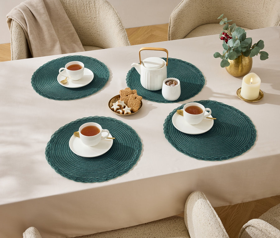 Vier Tassen Tee auf einem Tisch mit einer Tischdecke, Teekanne, Zuckerdose, Kekse und einer Kerze.