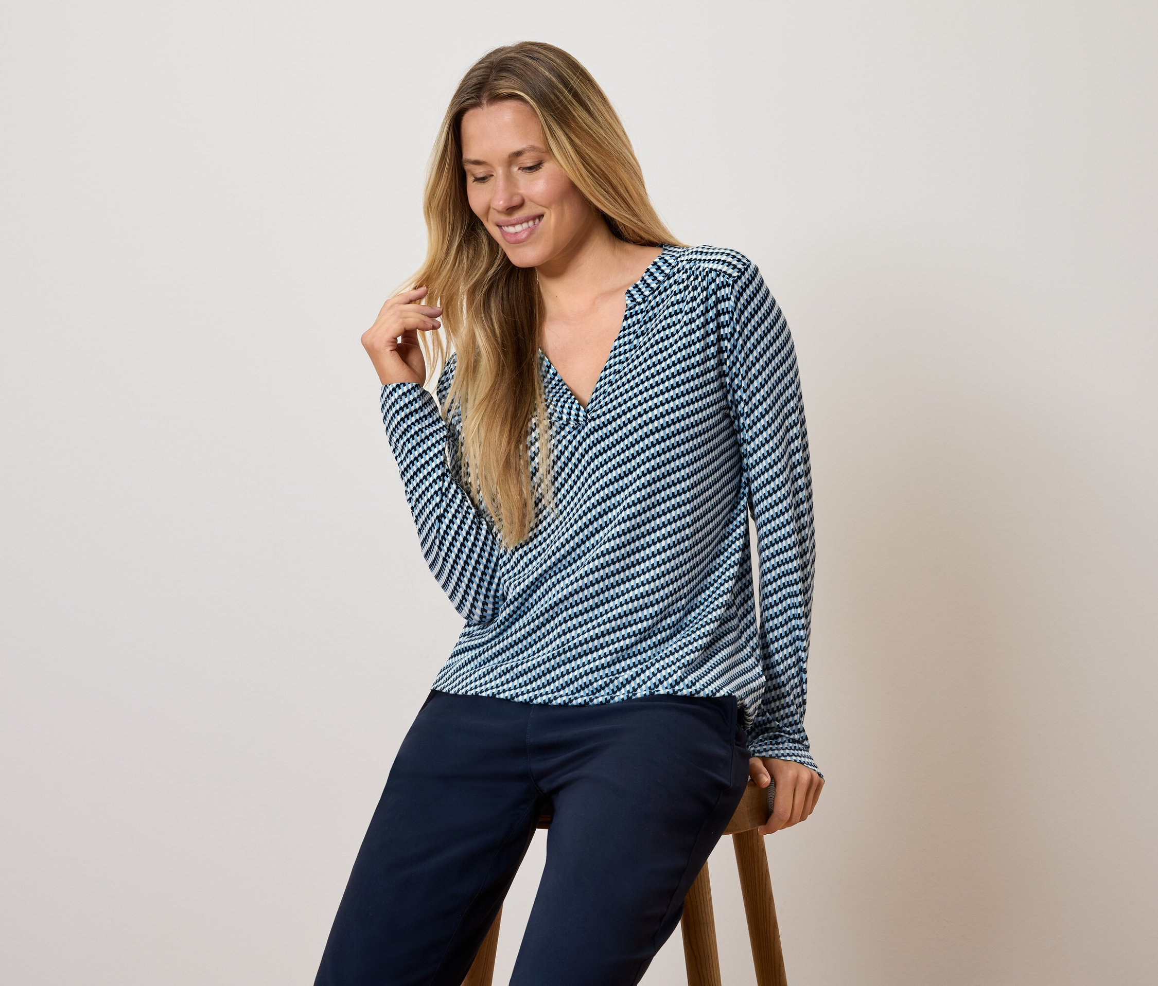 Frau sitzt auf einem Hocker, trägt ein blau-weiß gestreiftes Langarmshirt und dunkelblaue Hosen.