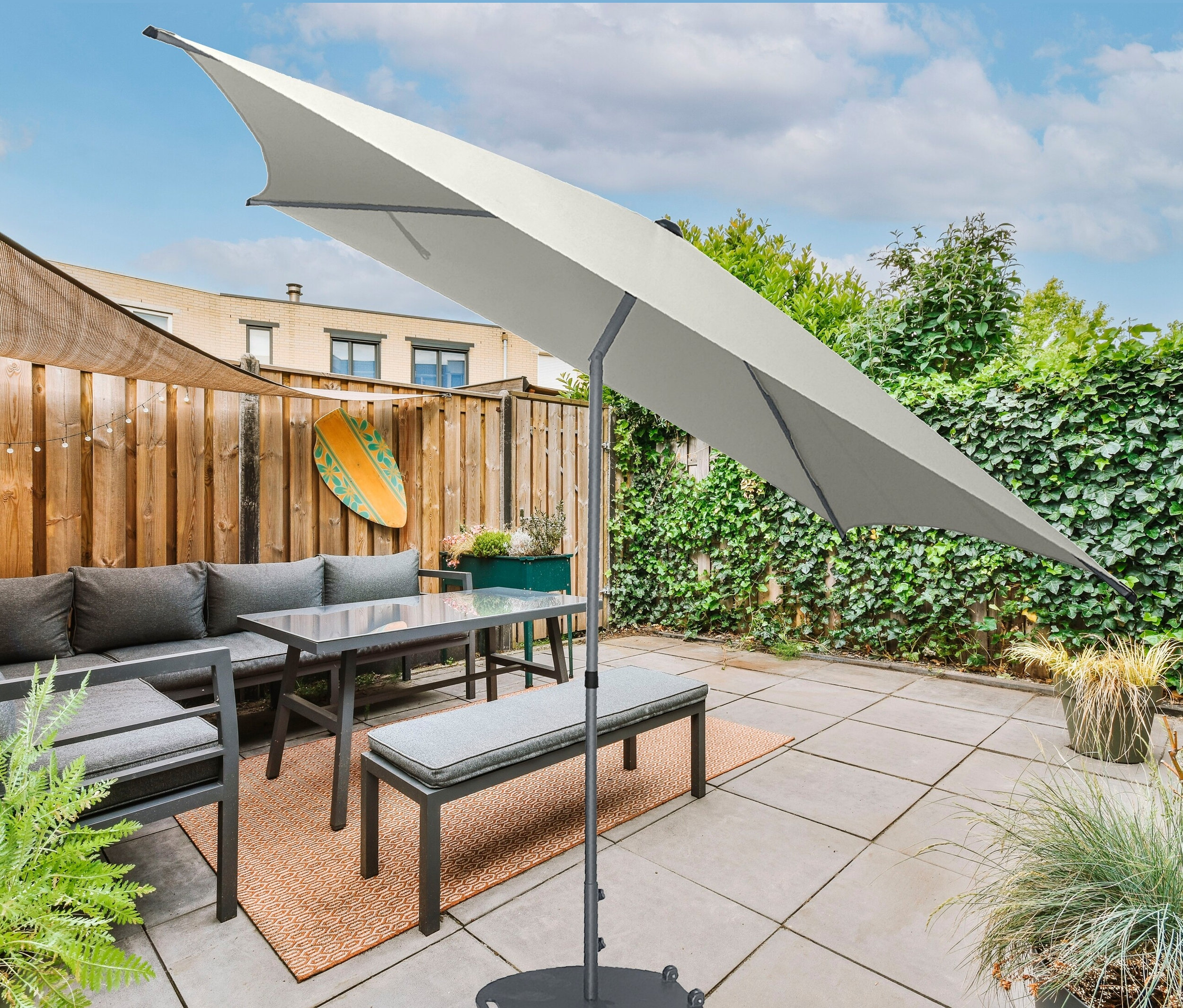 Graue Gartenmöbelgarnitur mit Leco Marktschirm überdacht eine Sitzecke.