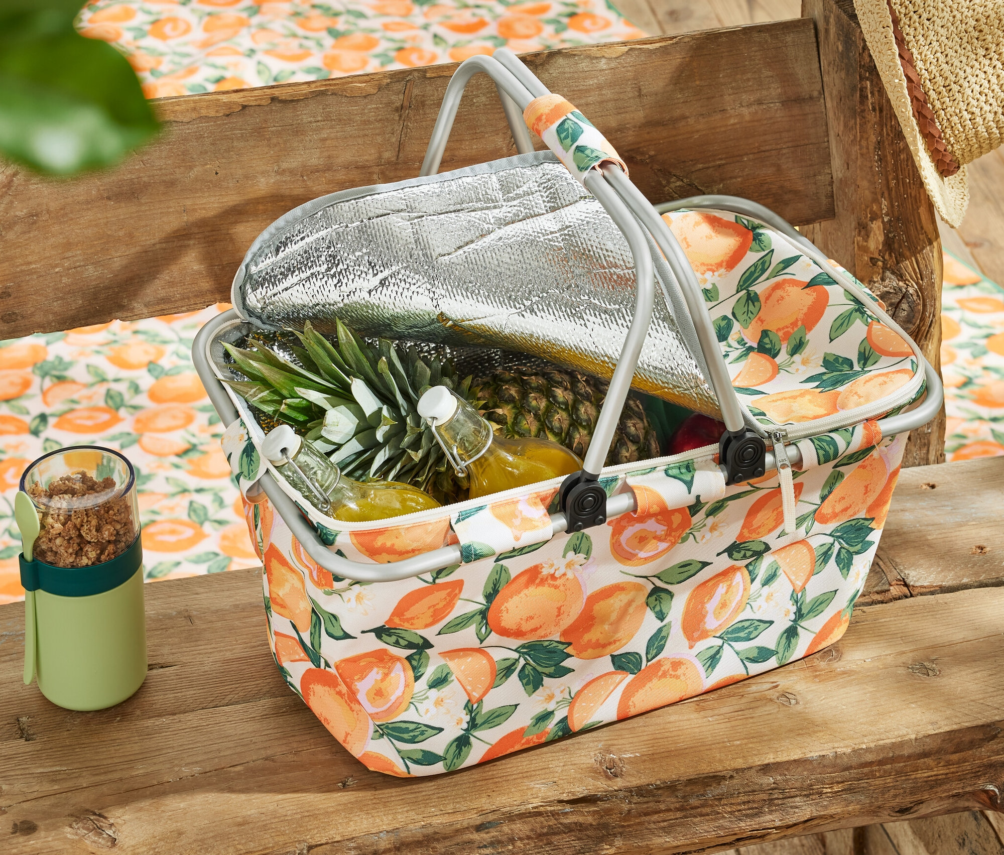 Kühlkorb mit Obst und Getränken auf einem Holztisch.