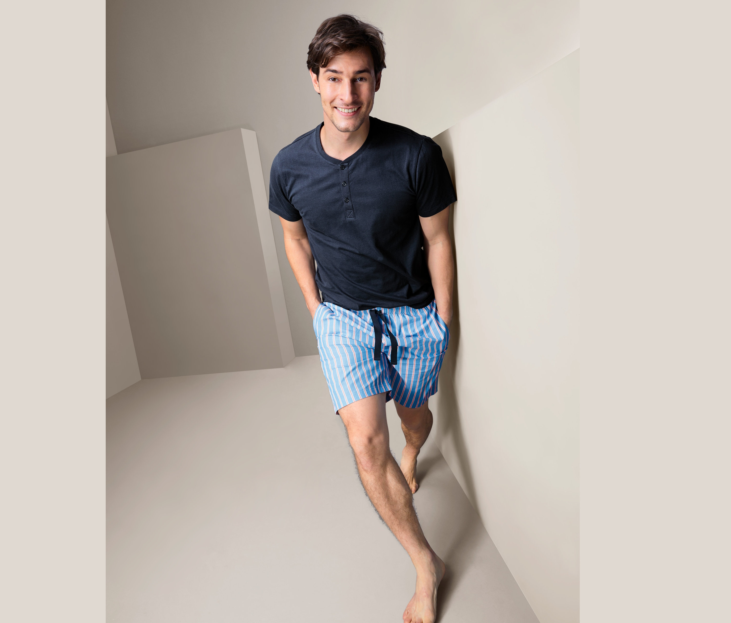 Ein Mann im Shorty-Pyjama steht in einer Ecke des Raumes.