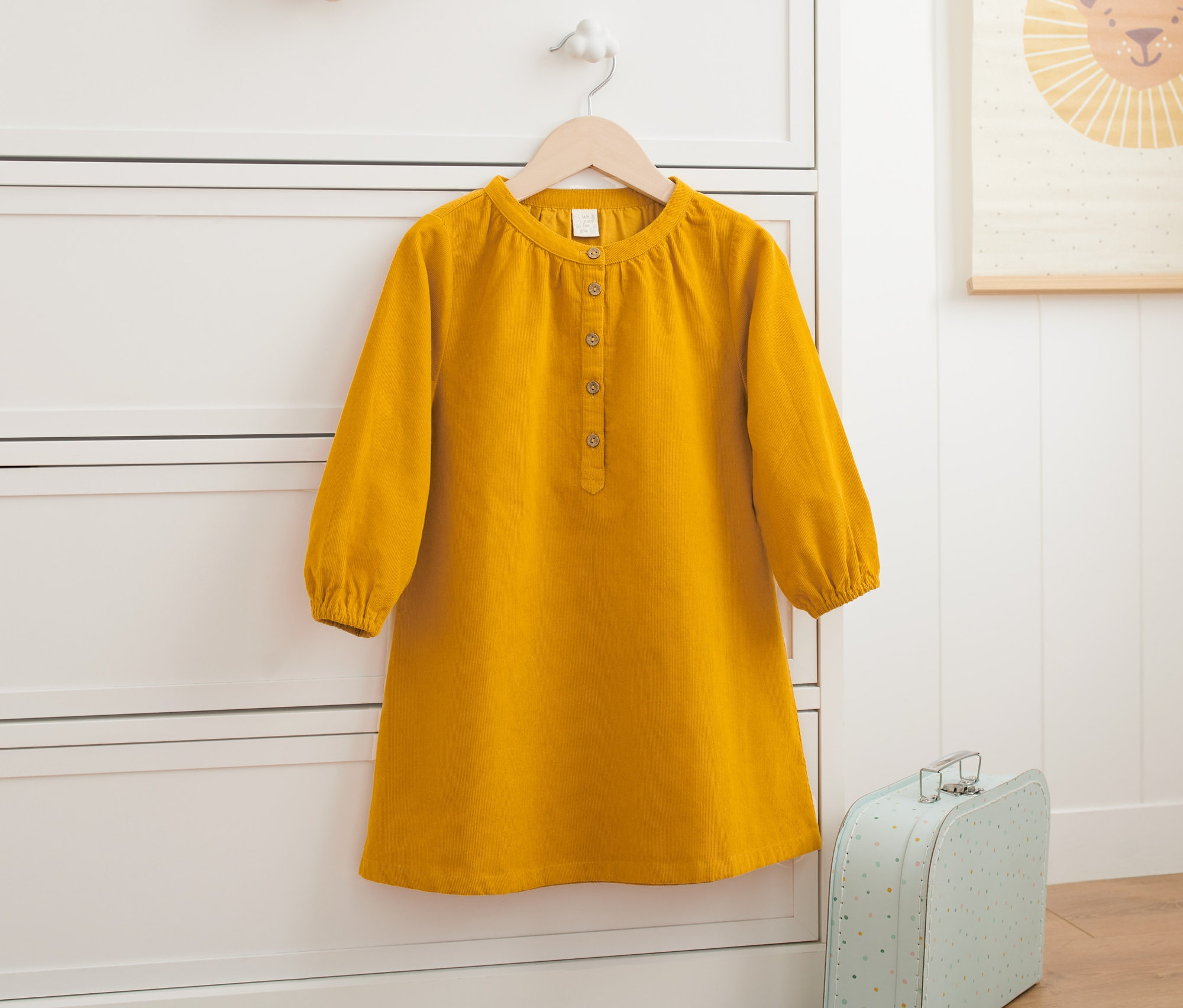 Ein gelbes Cordkleid hängt an einer weißen Kommode.