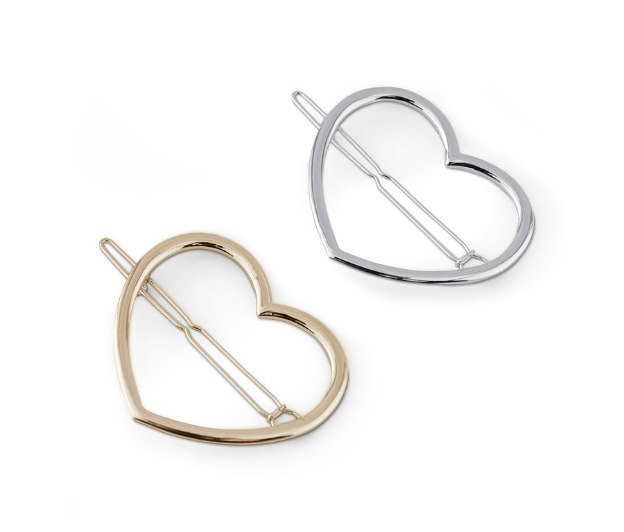 Zwei Haarspangen im Herzdesign, eine goldene und eine silberne, liegen auf einem weißen Hintergrund.