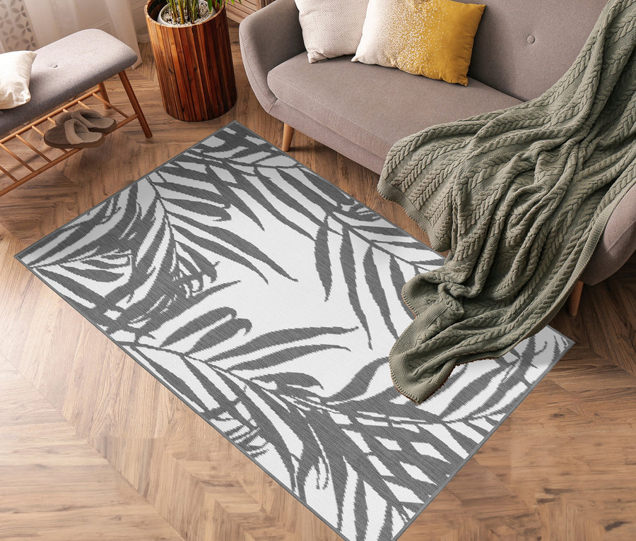 Wohnzimmer mit grauem Sofa, Topfpflanze und grauem Outdoor-Wende-Teppich »Palm Tree« mit Palmenblattmotiv.