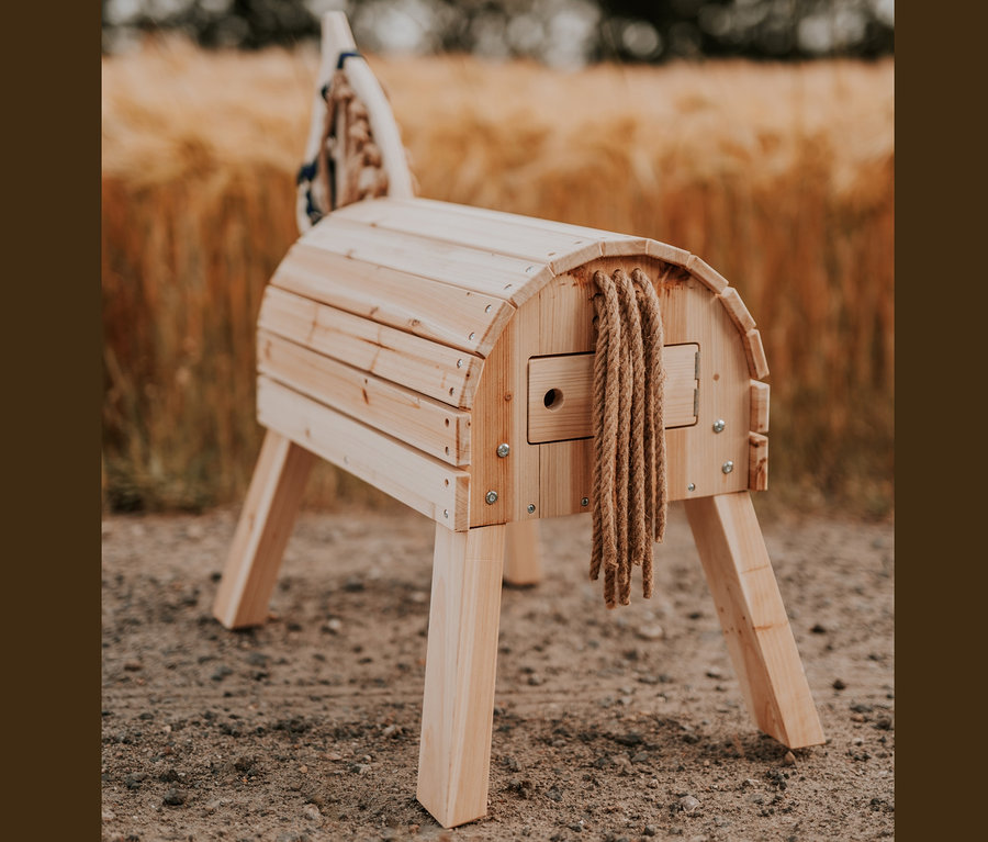 Das small foot Holzpferd, kompakt, steht auf dem Boden vor einem Getreidefeld.