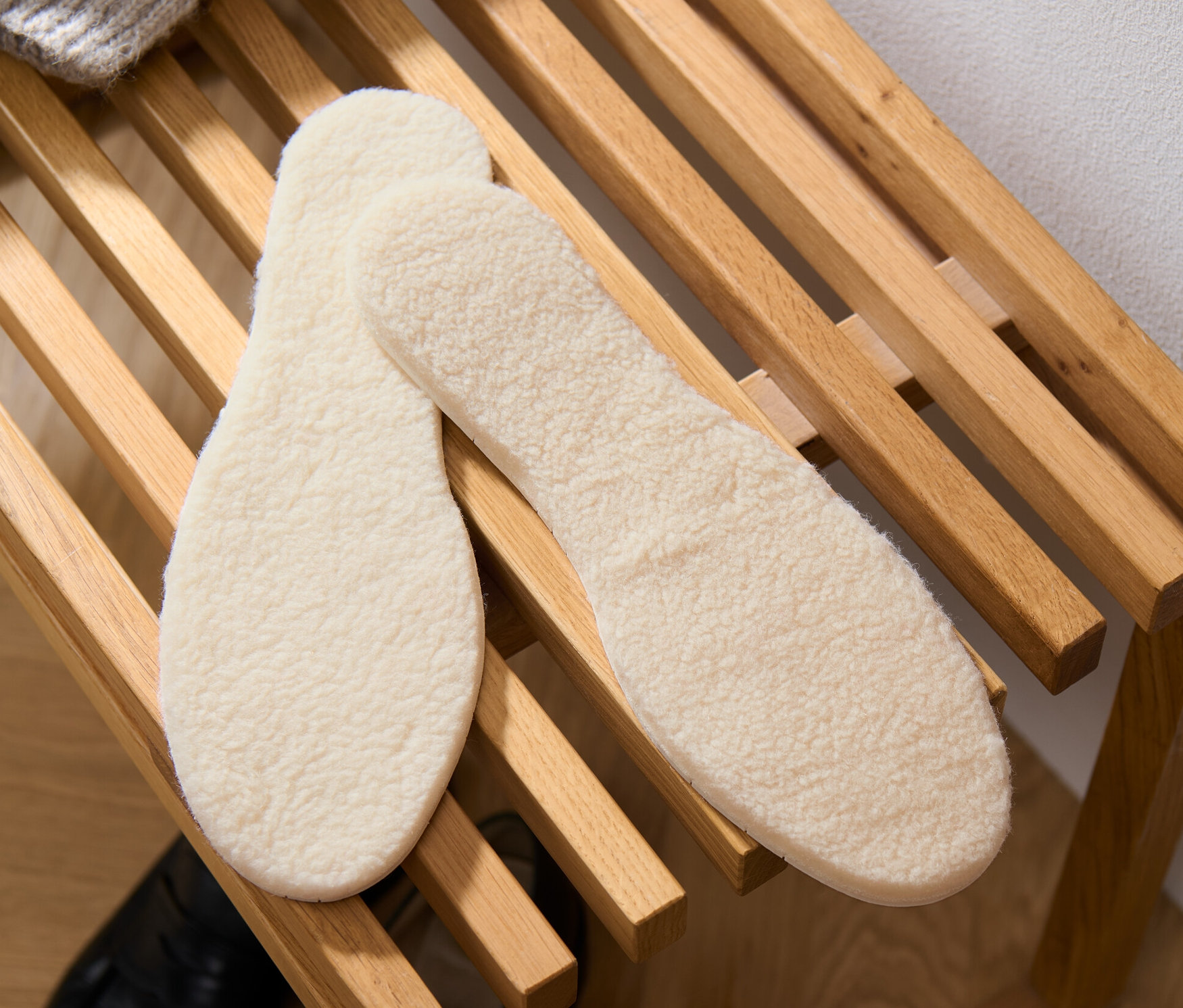 Zwei Paar Lammwoll-Einlegesohlen liegen auf einem Holzregal.