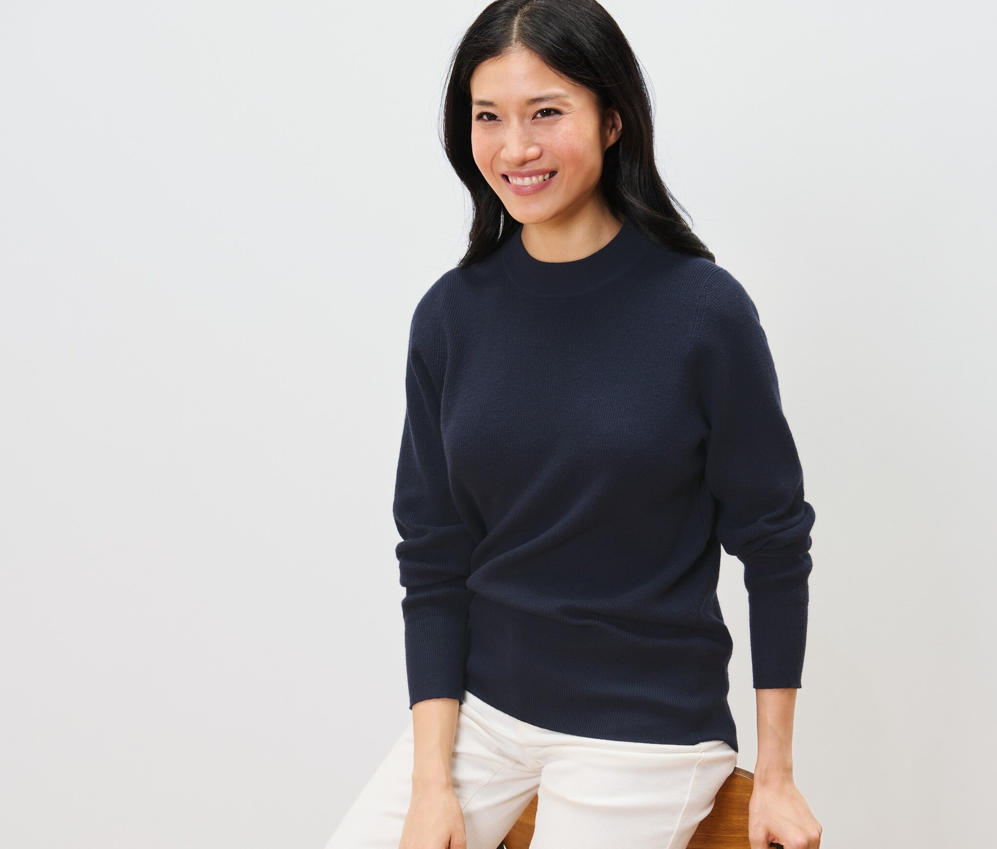 Frau sitzt und trägt einen dunkelblauen Feinstrickpullover.