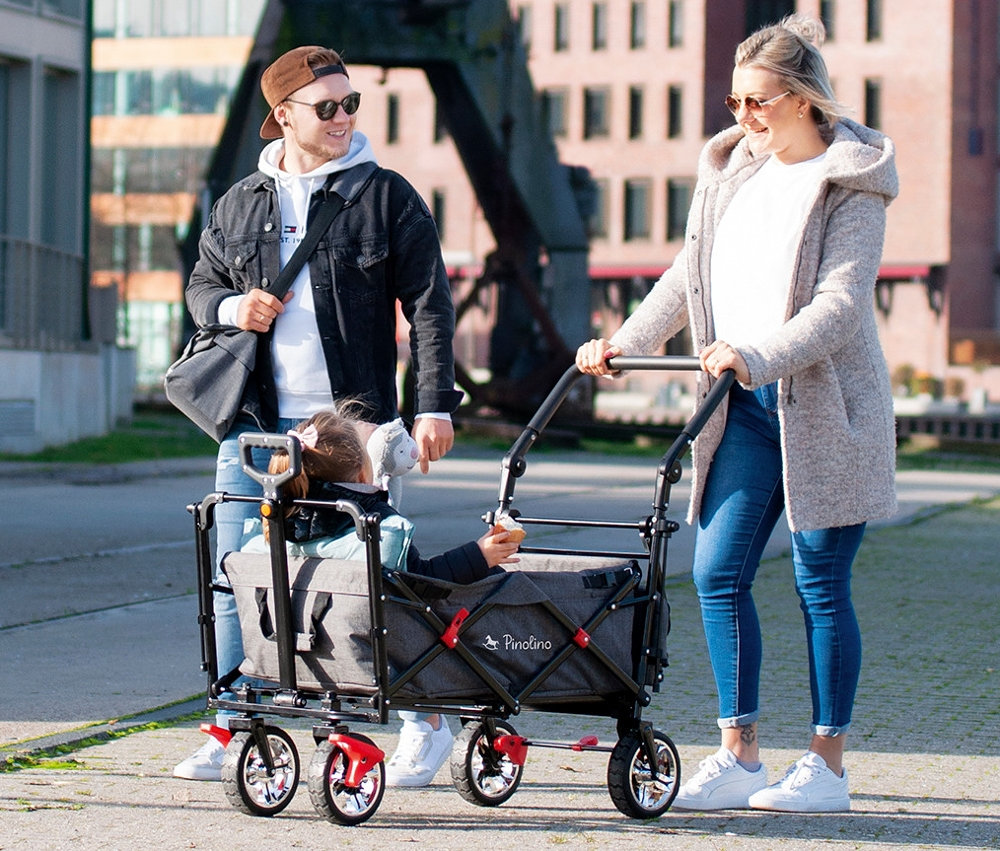 Eine Frau schiebt einen grauen Pinolino Klappbollerwagen Add Plus, in dem ein Kind sitzt, während ein Mann neben ihnen hergeht.