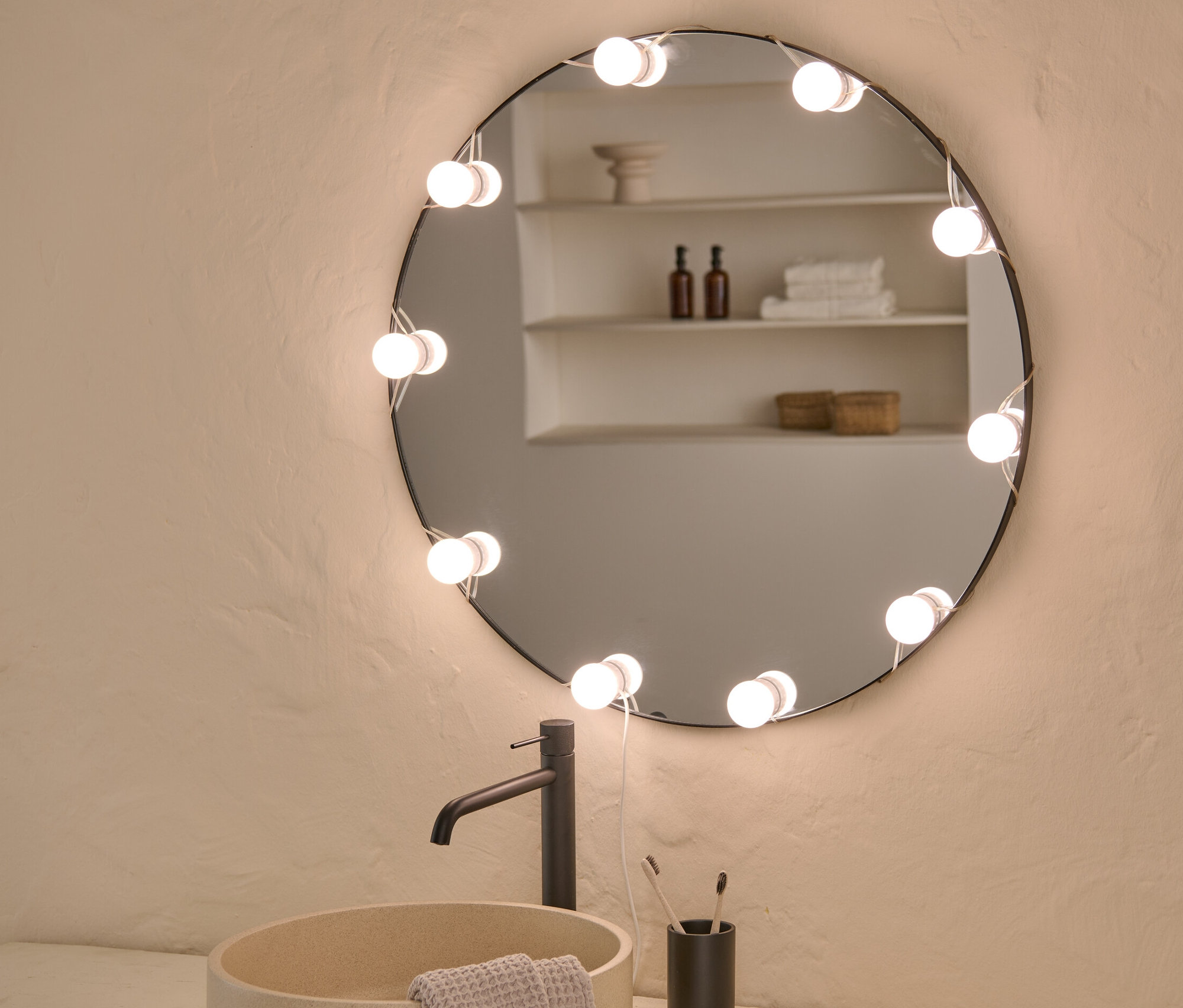 Badezimmer mit Waschbecken, Armatur und rundem Spiegel mit LED-USB-Lichterkette.