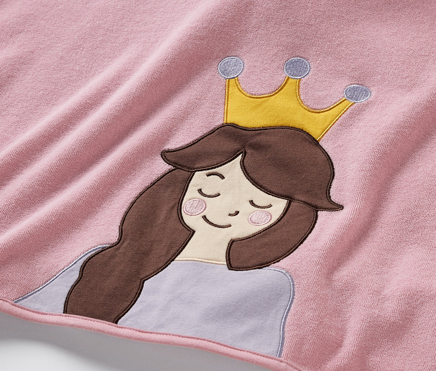 Detailansicht eines rosa Frottierponchos mit einer Applikation einer Prinzessin mit braunen Haaren und goldener Krone.