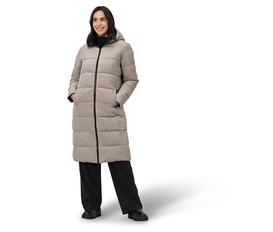 Frau posiert in einem beigen Daunenmantel und einer schwarzen Hose.
