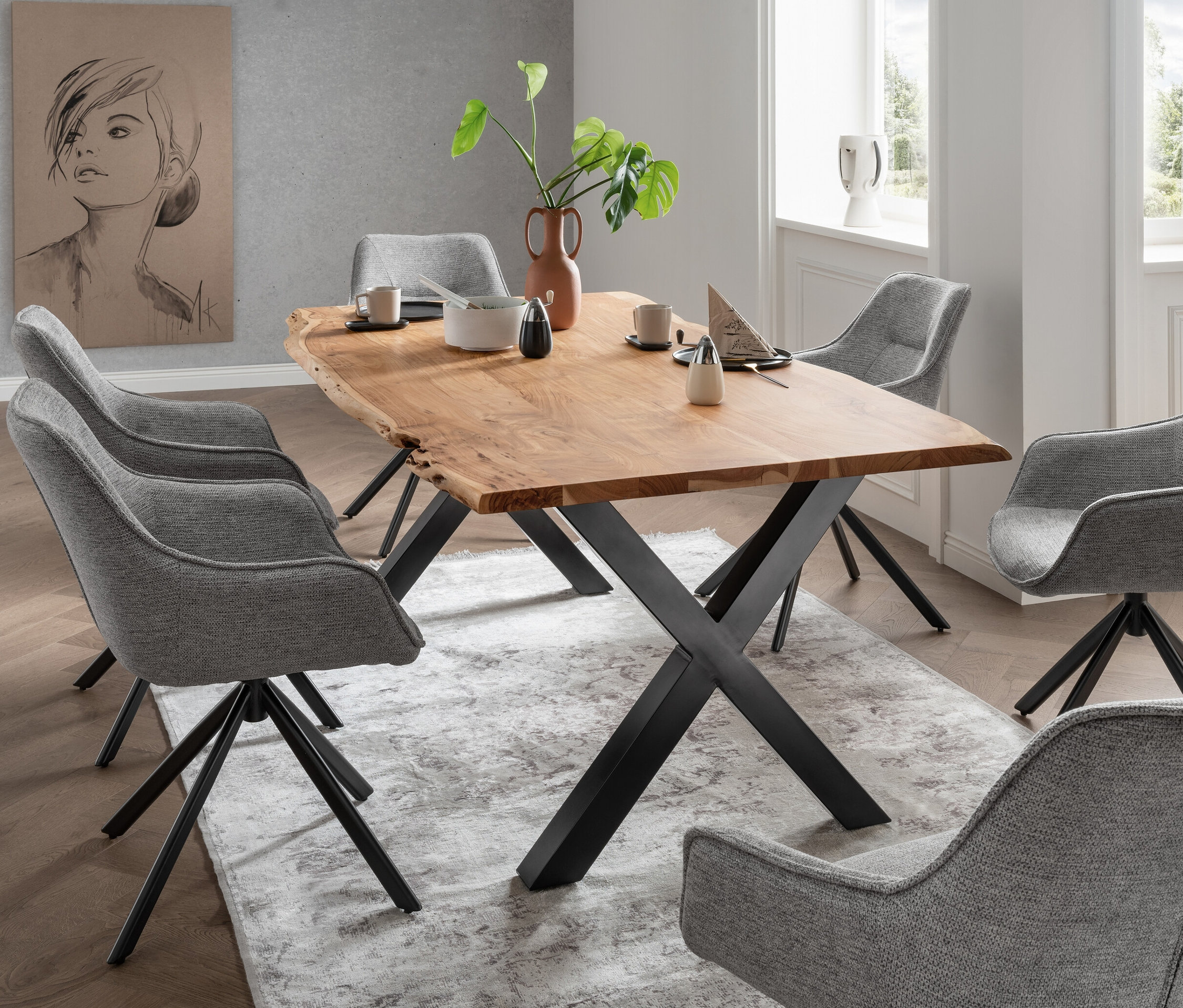 Ein Esstisch mit einer Holzplatte und Metallbeinen steht auf einem gemusterten Teppich, umgeben von sechs grauen Esszimmerstühlen.