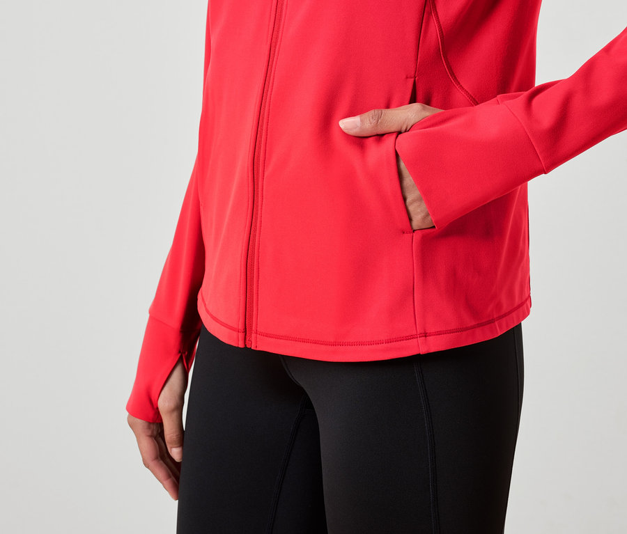 Frau hat Hand in der Tasche einer roten Jacke und trägt schwarze Leggings.