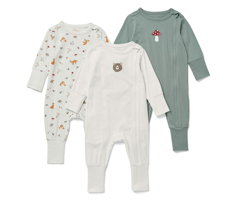 Drei langärmelige Baby-Overalls liegen nebeneinander. Einer ist weiß mit Tiermotiven, einer weiß mit einem Bären und einer grün mit einem Pilz.