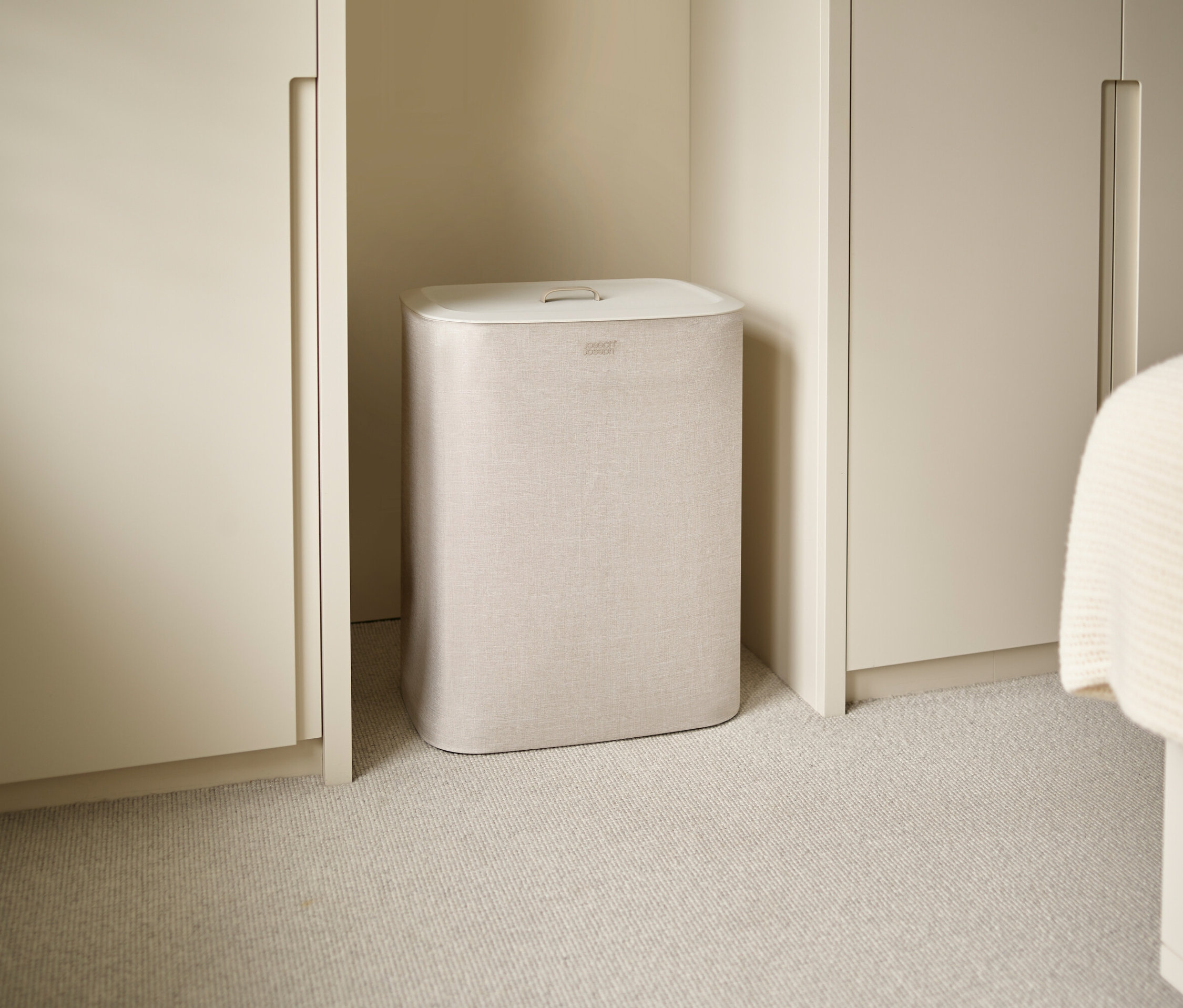 Ein beiger Joseph Joseph Wäschekorb steht zwischen Schränken auf einem beige Teppich.