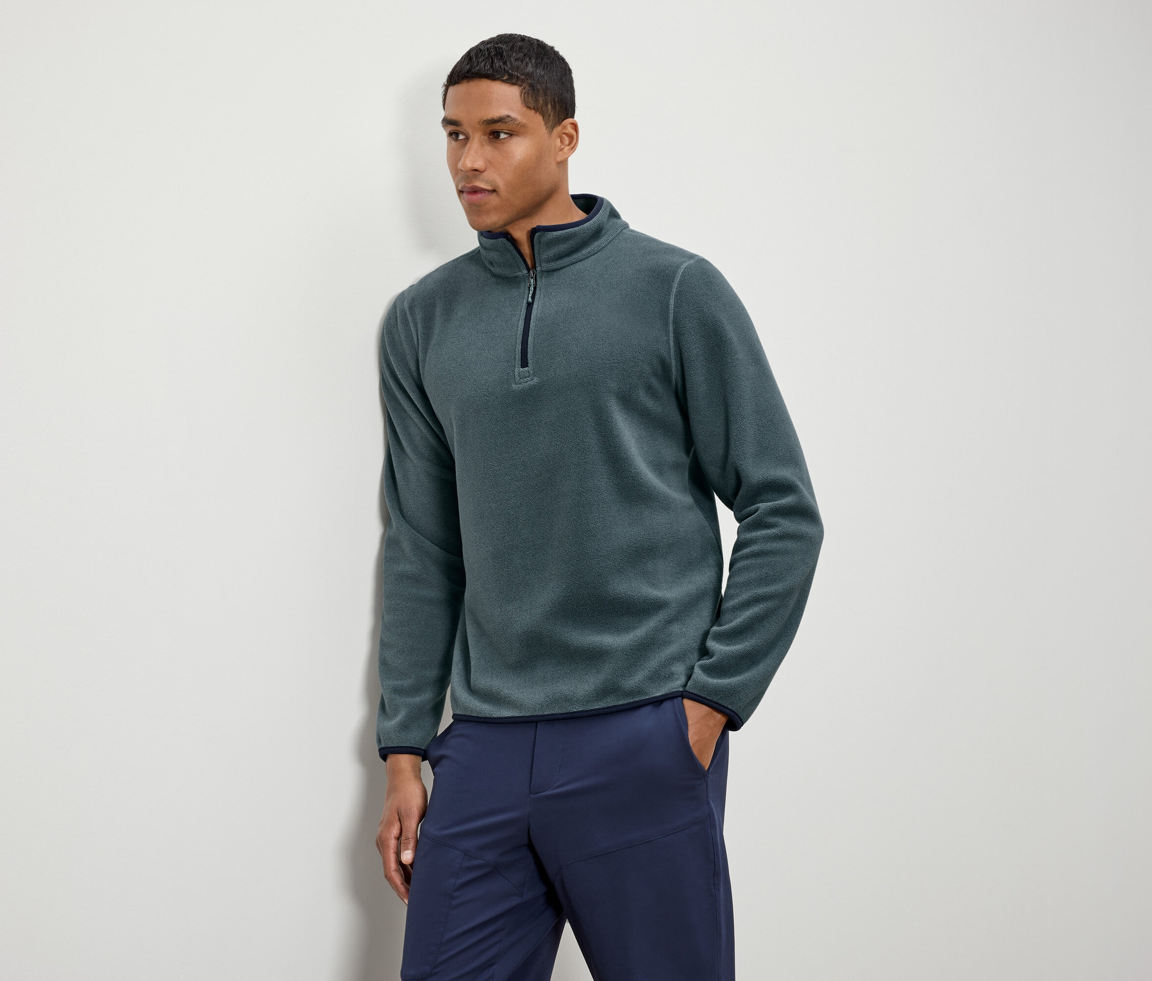 Mann trägt grünes Fleece-Halbarm-Oberteil mit marineblauen Hosen.