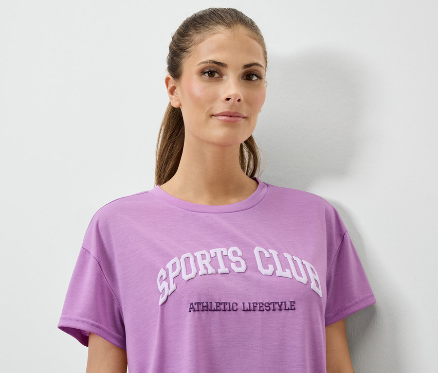 Frau trägt ein lila T-Shirt mit dem Aufdruck SPORTS CLUB ATHLETIC LIFESTYLE.