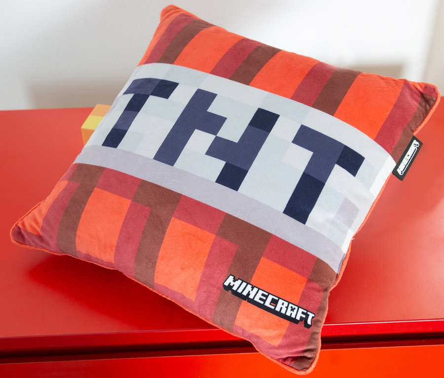 Ein quadratisches MINECRAFT TNT Dekokissen liegt auf einer roten Oberfläche.