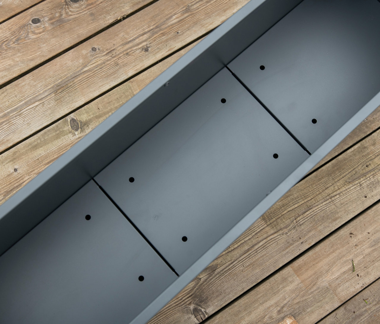 Ein anthrazitfarbener Pflanzkasten mit Einlegeboden (Höhe ca. 52cm) steht auf einem Holzboden.