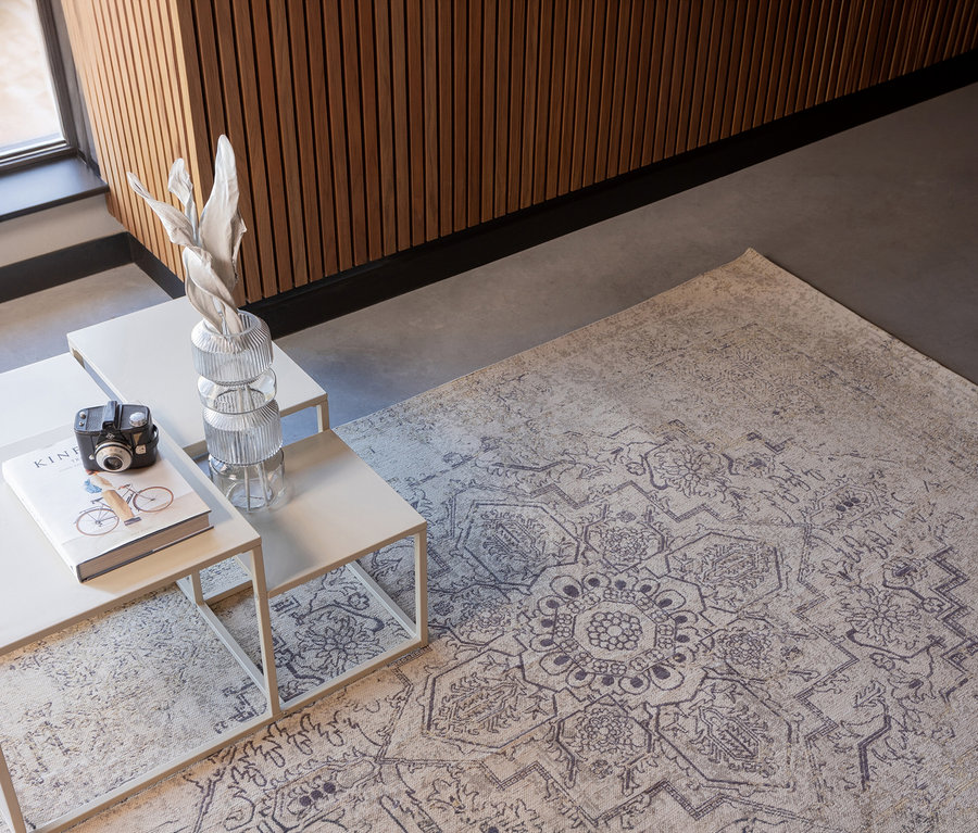 Auf grauem Boden liegt der mehrfarbige Woood Teppich »Eric« (170 x 240 cm). Darauf stehen drei Tische mit Deko.