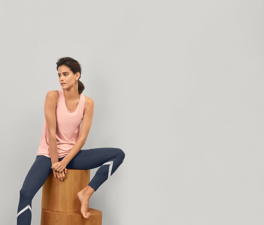 Frau sitzt auf Holzblöcken und trägt eine blaue Sporttight »Soft Touch« und ein Sporttop.