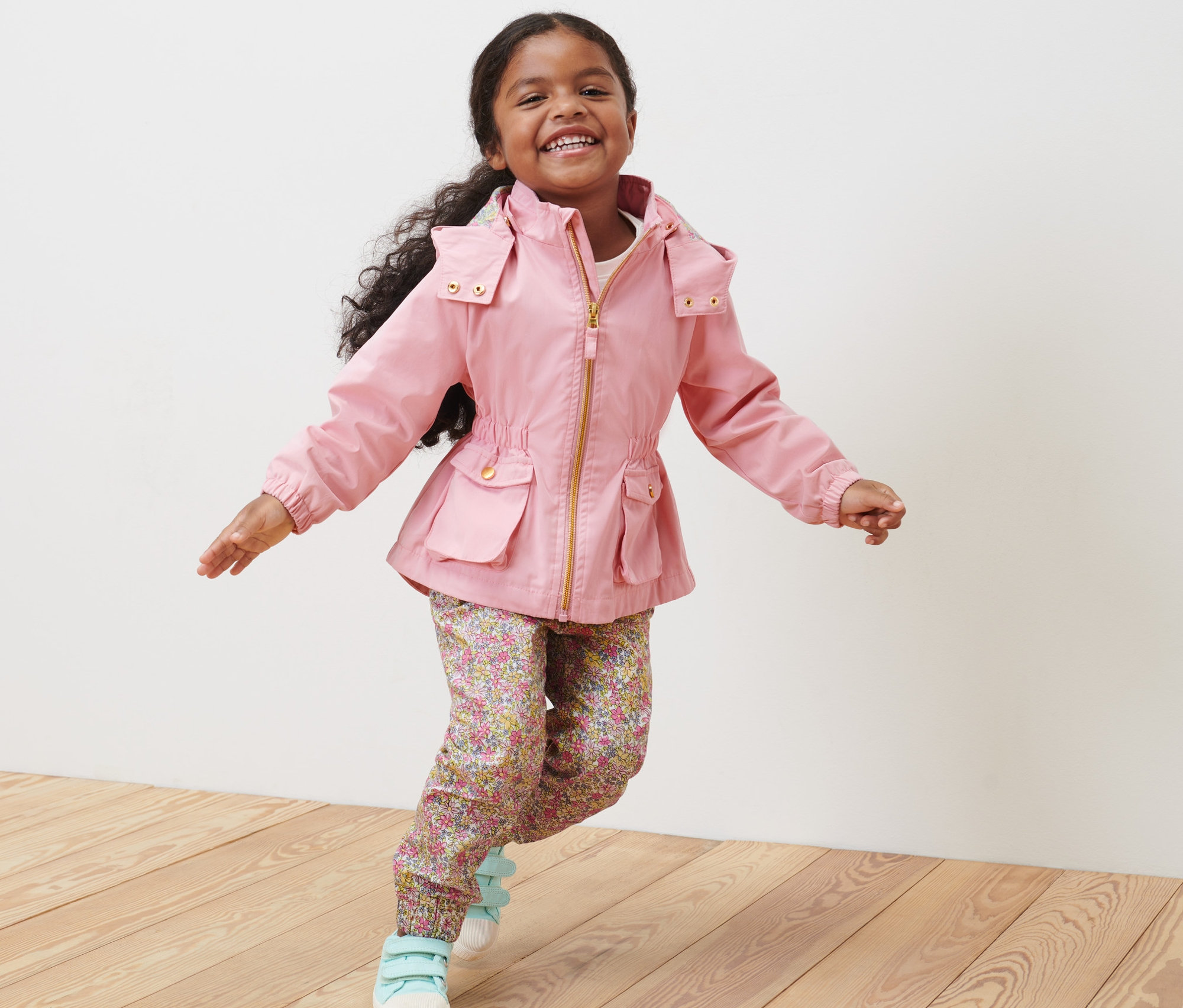 Lächelndes kleines Mädchen trägt eine Kleinkind-Parka und rennt auf einem Holzboden.