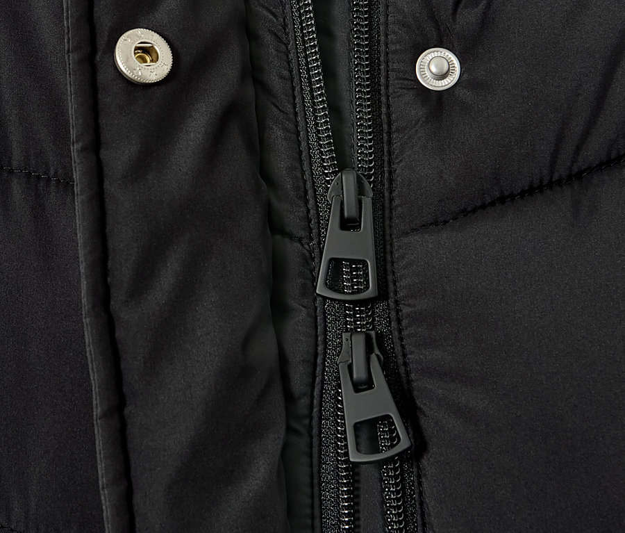 Detailansicht eines schwarzen Steppmantels mit Kapuze, der Reißverschluss und Knöpfe zeigt.