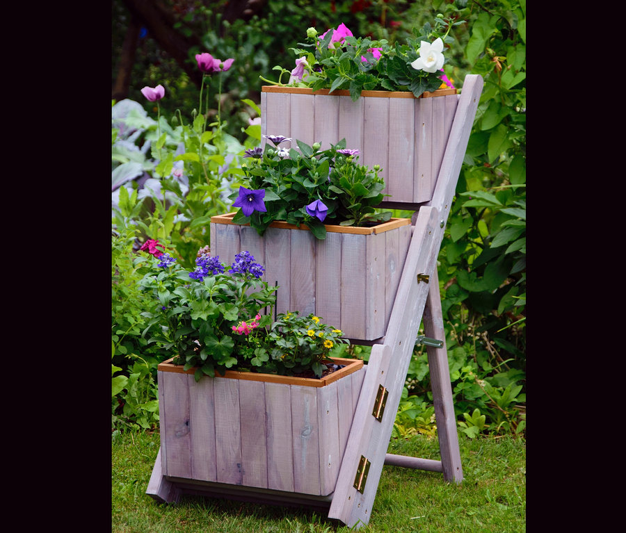 Eine graue Pflanztreppe mit 3 Pflanzkästen steht draußen auf einer Wiese.