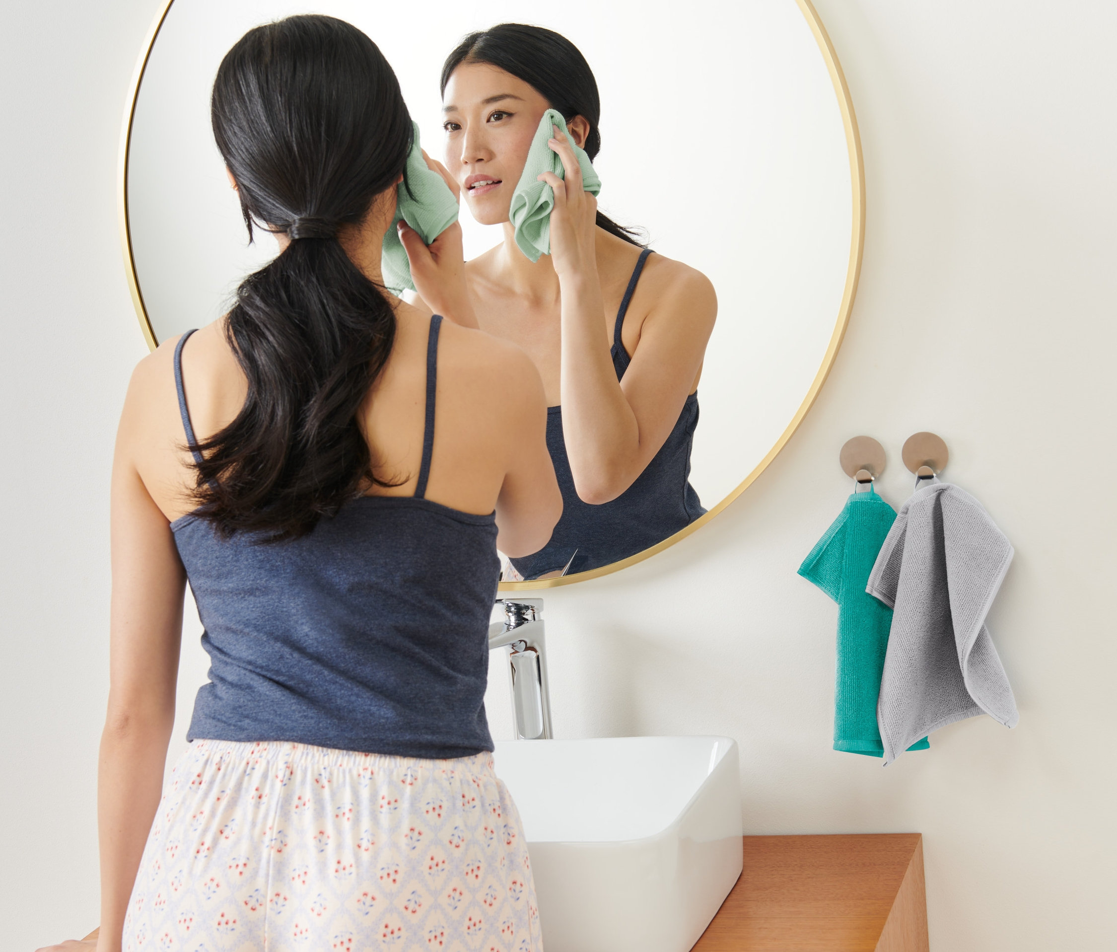 Frau reinigt ihr Gesicht mit einem 3er-Pack Kosmetiktüchern aus Microfaser vor einem Spiegel.