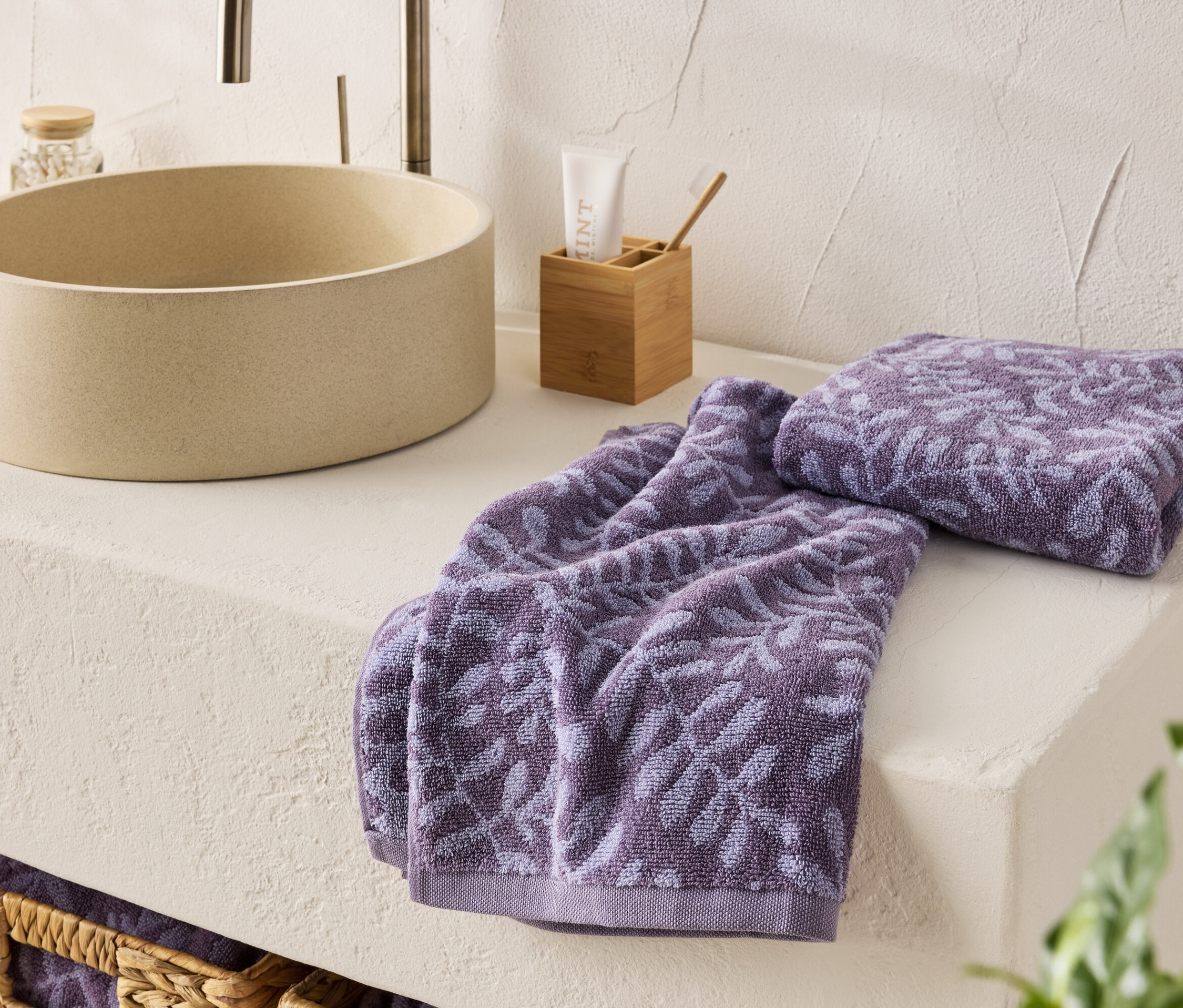 Zwei lila Handtücher mit Blumenmuster liegen neben einem Waschbecken.