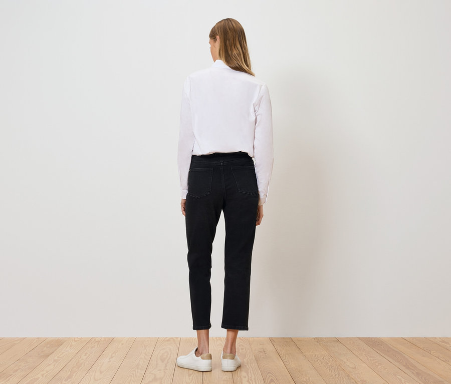 Von hinten ist eine Frau in einem weißen Hemd, schwarzen Hosen und weißen Schuhen zu sehen.