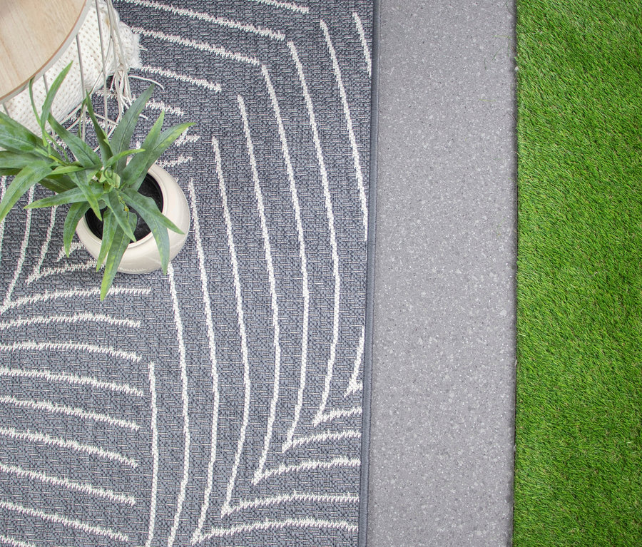 Draufsicht eines grauen Teppichs mit weißem Blattmuster, einer Topfpflanze, Beton und Kunstrasen.