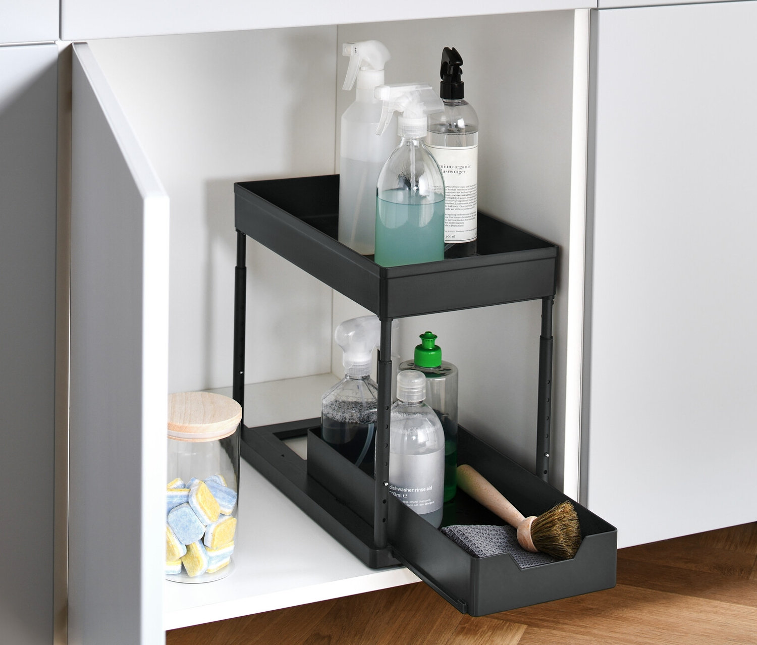Ein offener, weißer Schrank mit einem höhenverstellbaren Schrankauszug, der Reinigungsmittel enthält.