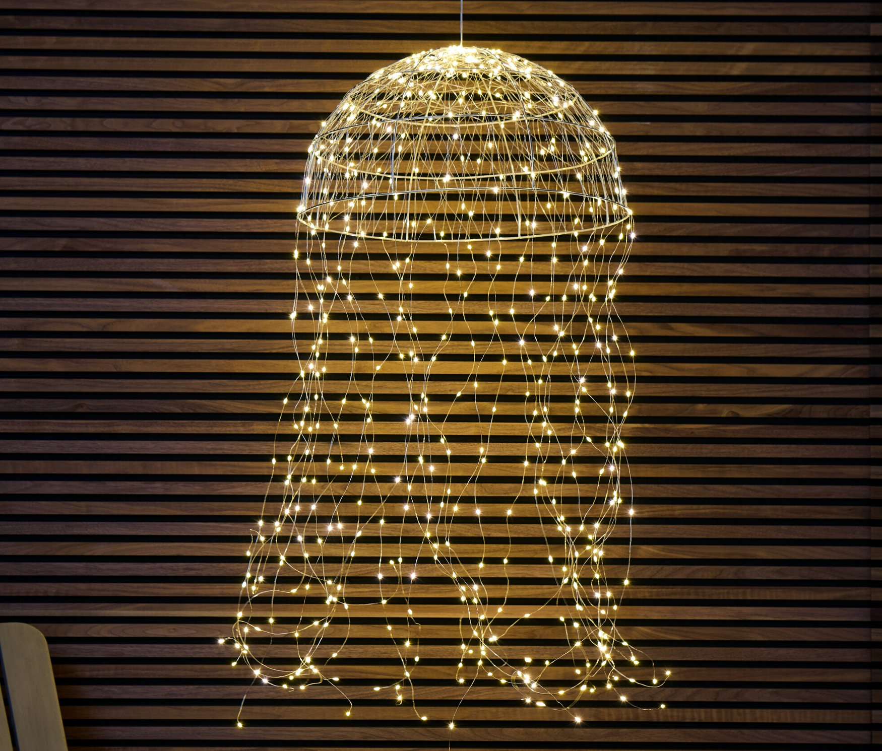 Eine große hängende LED-Halbkugel mit einem Lichterbündel hängt vor einer Holzwand.