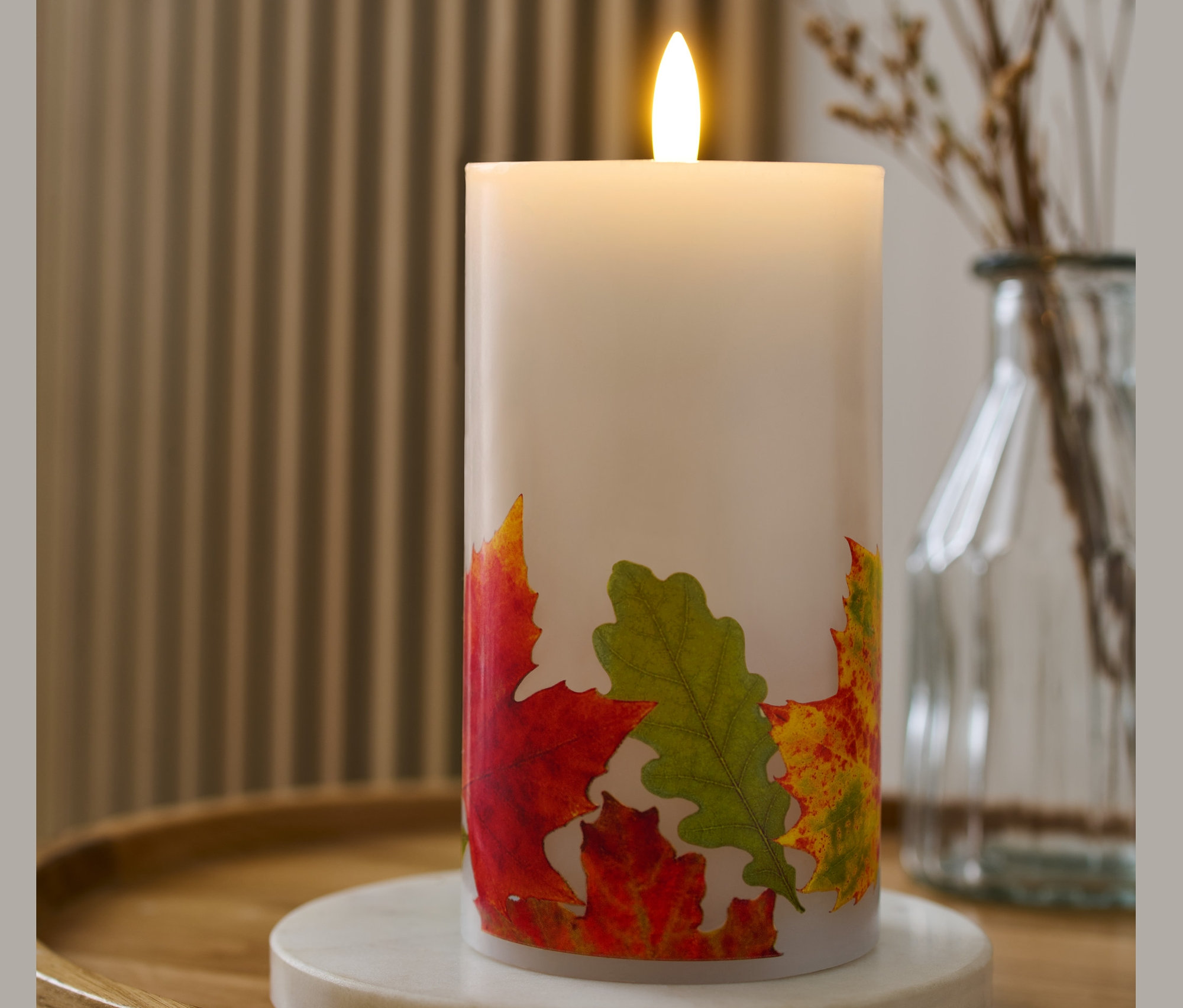 LED-Echtwachskerze mit Blätter-Print steht auf einem Tisch.