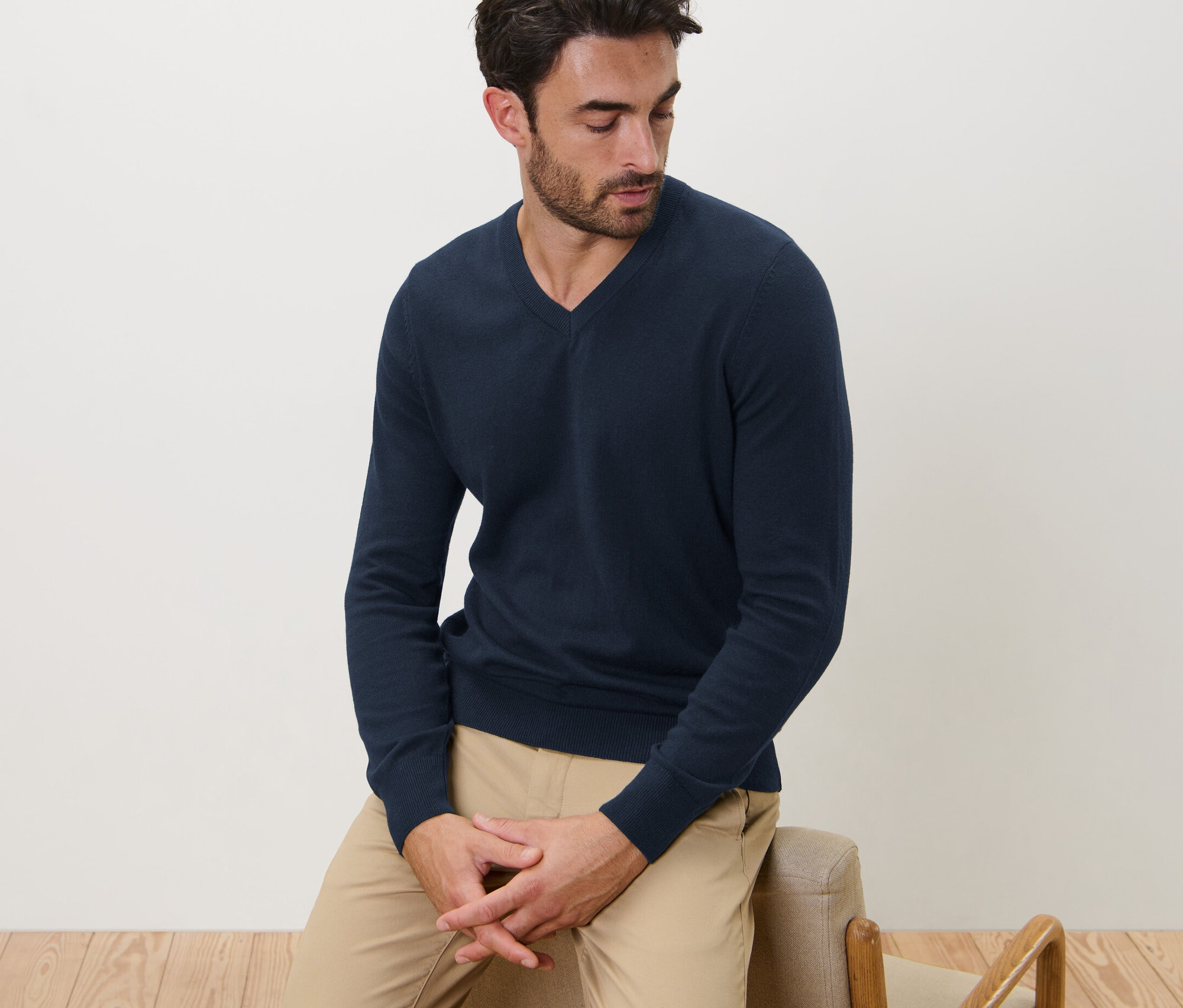 Mann sitzt und trägt einen navy Pullover mit V-Ausschnitt.