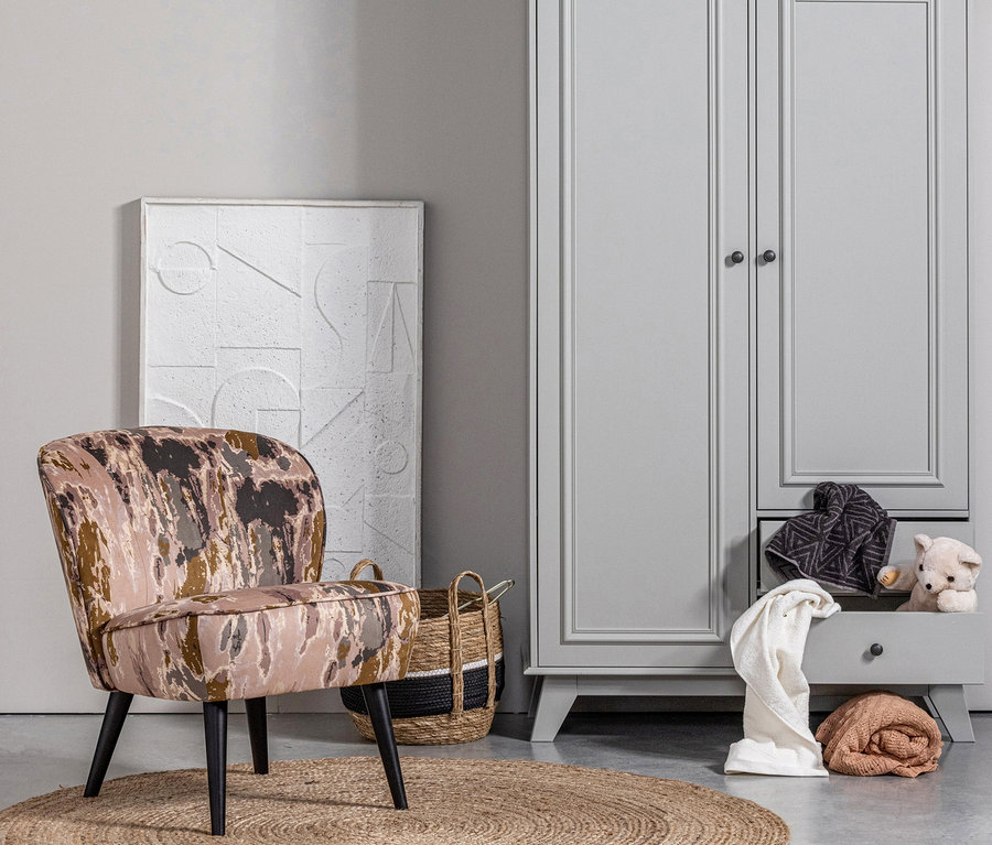 Ein naturfarbener Woood Teppich »Ross« 150 cm liegt auf dem Boden, daneben stehen ein Sessel und ein grauer Schrank.