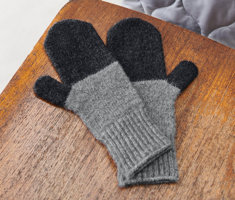 Ein Paar hellgraue Strick-Fäustlinge liegen auf einem Holzstuhl.