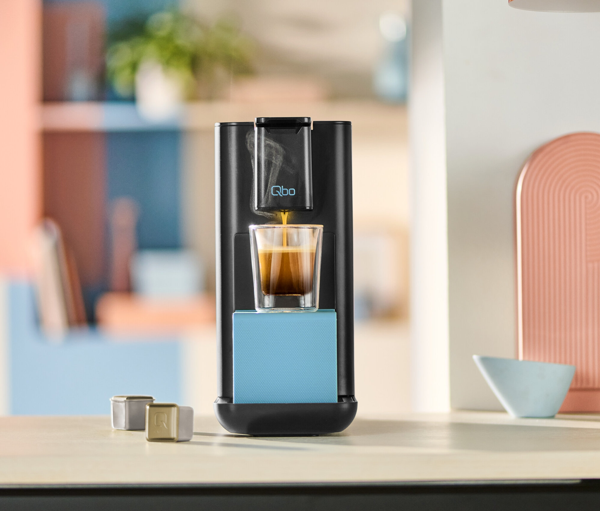 Qbo ICONIC x Pantone Special Edition Sky Blue Kaffeemaschine befüllt ein Glas mit Kaffee.